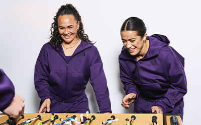 Two smiling individuals wearing purple hooded jackets stand in front of a plain white background.