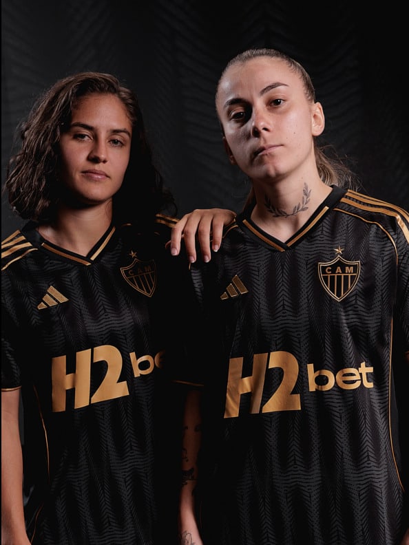Two individuals wearing black and gold soccer jerseys with the text "H2bet" prominently displayed, standing against a dark background.