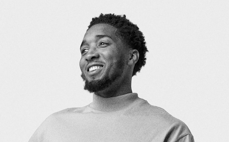 A close-up portrait of a smiling man with a beard and short, spiky hair against a plain white background.
