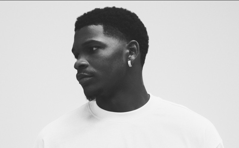 A close-up portrait of a young man with a serious expression, set against a plain white background.