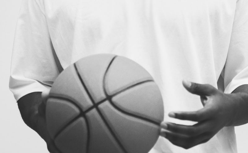 A basketball is held in the foreground against a blurred, white background.