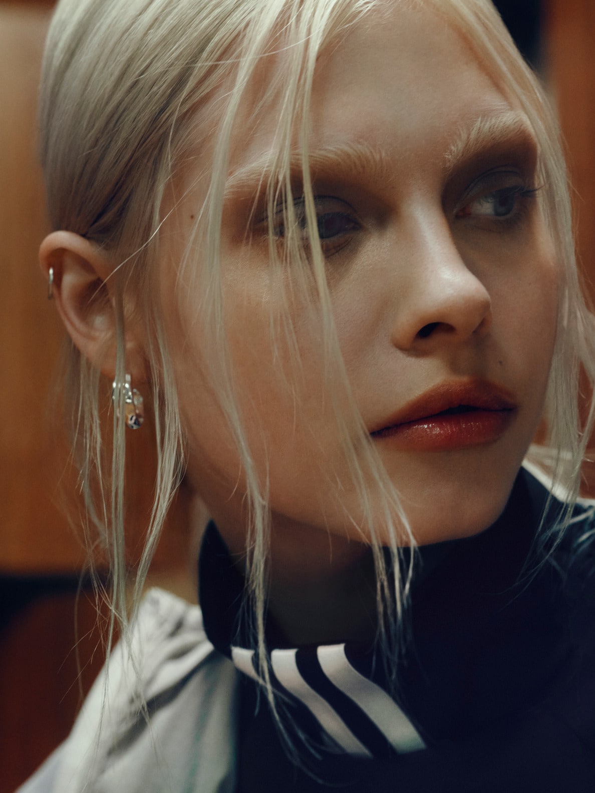 The image depicts a close-up of a woman's face, with her blonde hair blowing in the wind and a serious expression on her face. The background appears to be a plain, dark-colored surface.