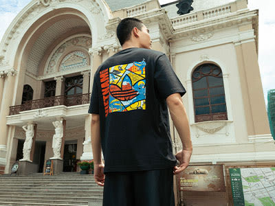 A person wearing a black t-shirt with a colorful abstract design on the back, standing in front of a grand, ornate building with arched windows and intricate architectural details.