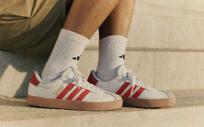 The image shows a pair of white and red sneakers with white socks, resting on a tiled floor.