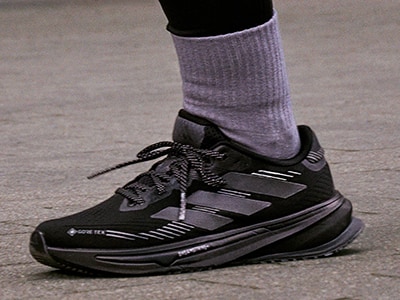 Ett par svarta och grå sportskor med snören, burna av en person som står på en betongyta.