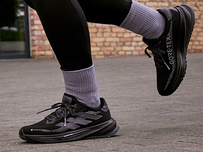 De afbeelding toont iemands onderlichaam in een zwarte legging en grijze sokken, samen met een paar zwarte en witte sportschoenen op een stenen stoep.