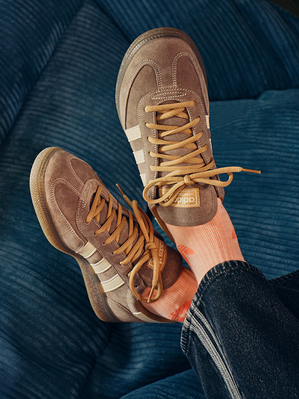 Bilden visar ett par bruna och beige sneakers med snören, som vilar på en blå och vit randig bakgrund.