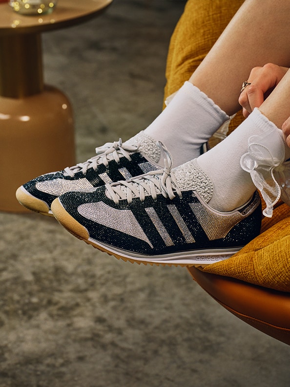 De afbeelding pronkt met een paar sneakers met retro stijl en een opvallend zwart-wit design, rustend op een behaaglijke, mosterdkleurige stoel tegen een vervaagde achtergrond.