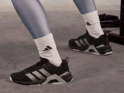 De afbeelding toont een paar benen die witte sokken en zwarte sportschoenen dragen en op een betonnen oppervlak staan.