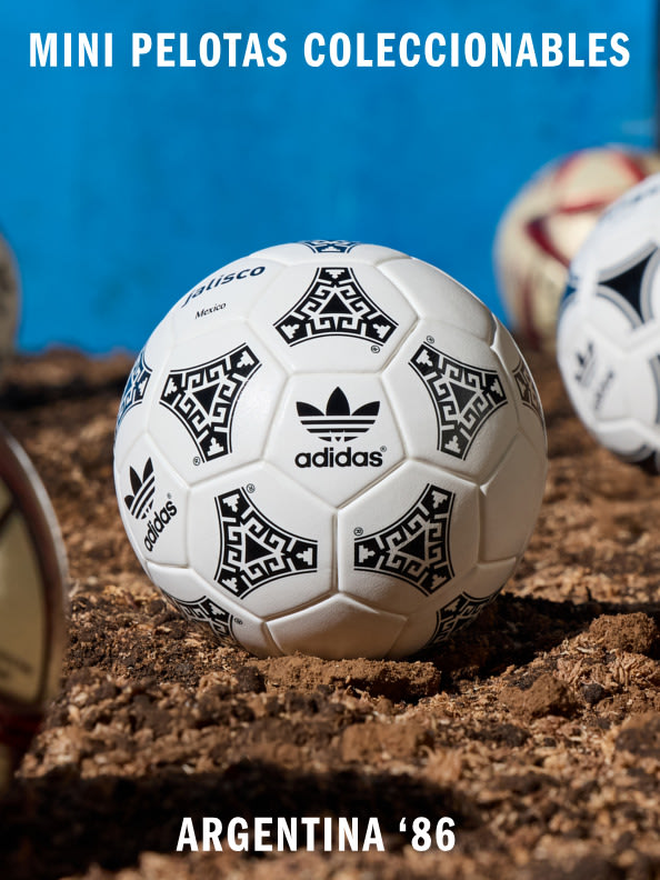 A small, collectible soccer ball with the Adidas logo and "Argentina '86" text sits on a textured, earthy surface against a vibrant blue background.