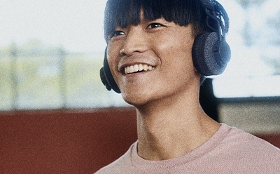 A smiling young person with dark hair wearing headphones against a blurred background.