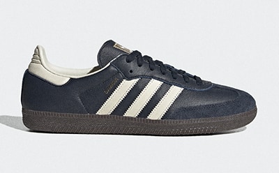 A pair of black and white Adidas sneakers with a gum sole is the focus of the image, set against a plain white background.