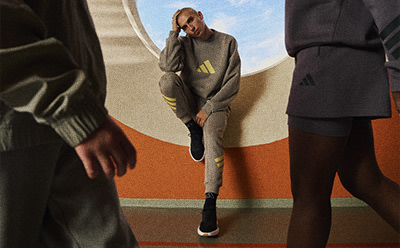 The image depicts a person wearing a gray hooded sweatshirt and black pants, standing in a hallway with a colorful, abstract background.