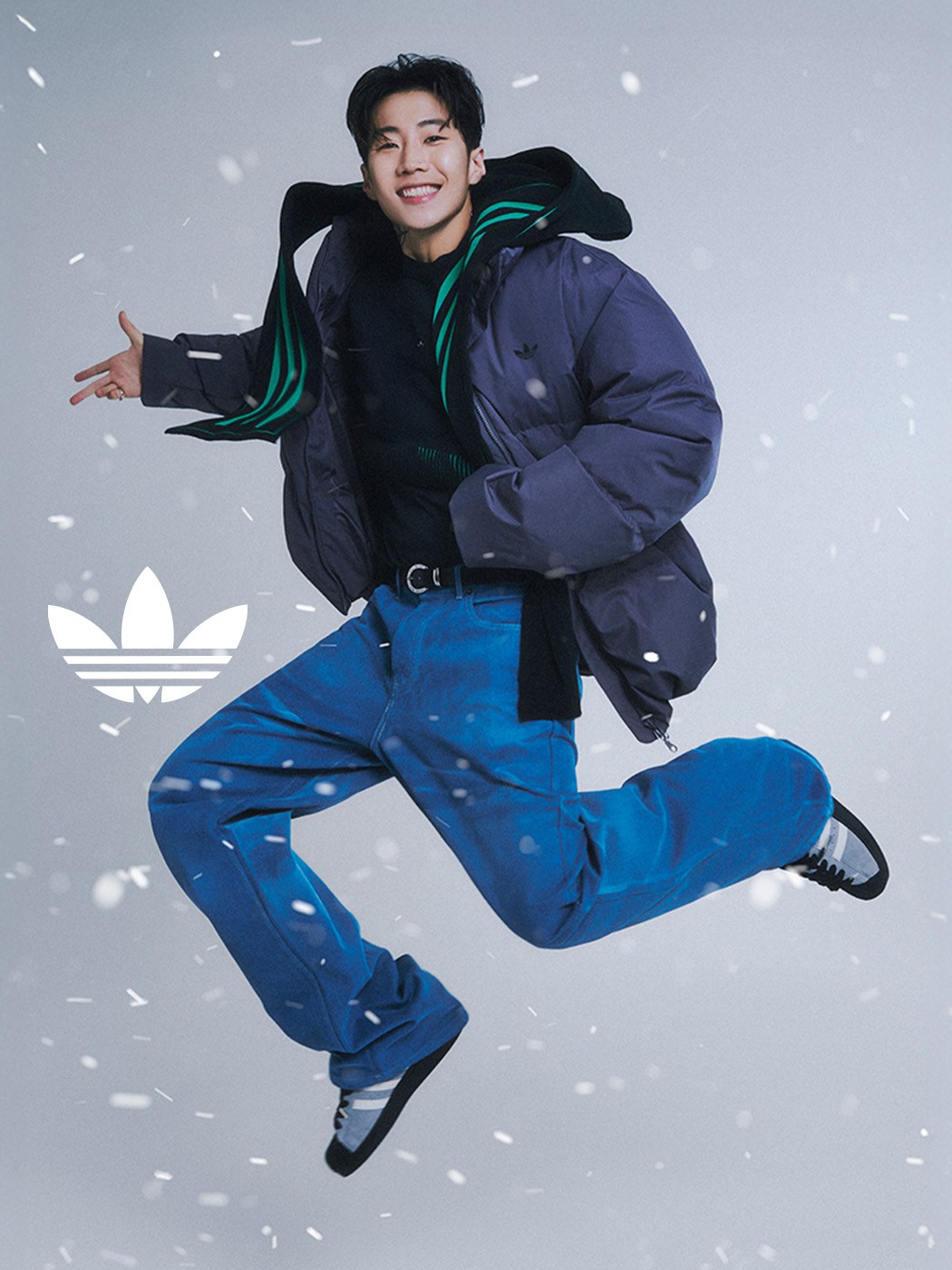 A person wearing a black jacket and blue pants is jumping in the air against a snowy background.