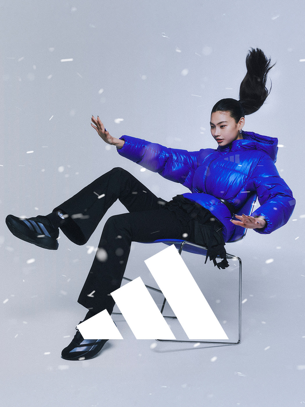 A person in a vibrant blue puffer jacket is sitting on a white cube-shaped object, with snowflakes falling in the background.