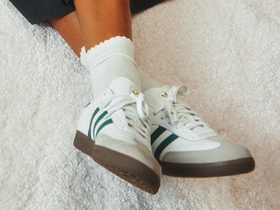 Hvite sneakers med grønne og svarte striper på en hvit, myk overflate.