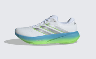 A white, green, and blue athletic shoe with a distinctive sole design is the focus of the image, set against a plain background.