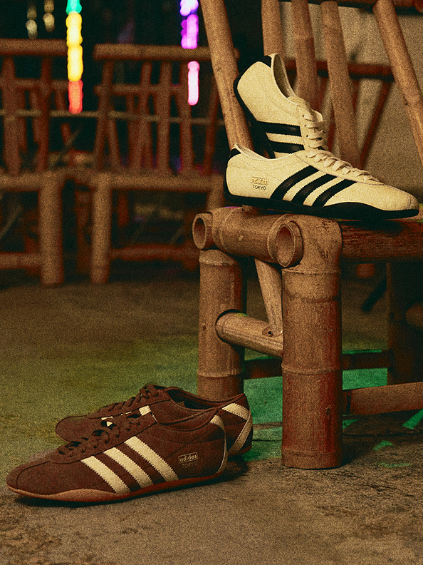 The image shows a pair of Adidas sneakers on a wooden bench, with a second pair of sneakers visible in the background, set against a backdrop of colorful lights.