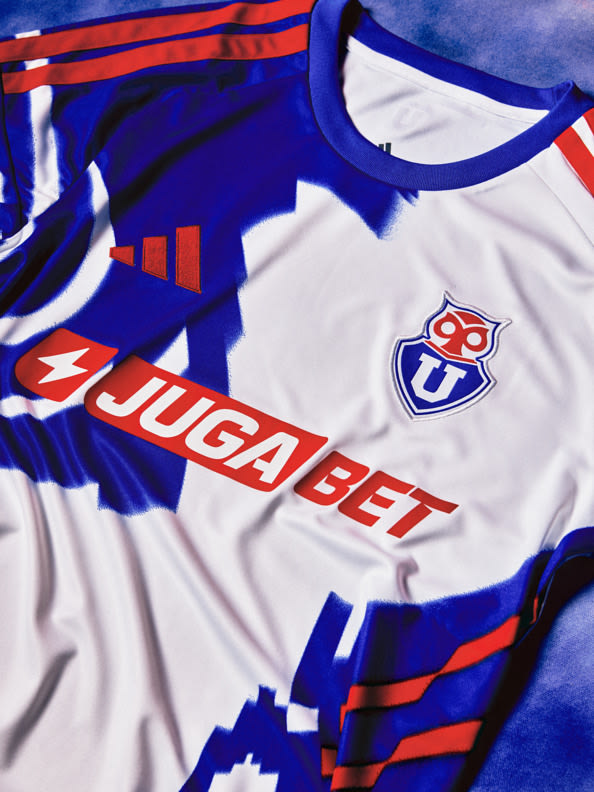 The image depicts a soccer jersey with the text "JUGADET" prominently displayed, set against a vibrant blue and red background.