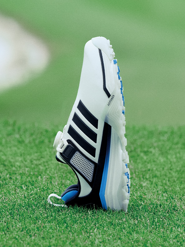A white and black athletic shoe with blue accents sits on a lush green grass surface.