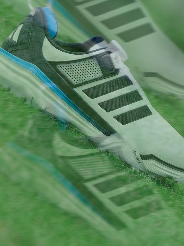 A close-up view of a sports shoe with a green and blue design, resting on a grassy field.