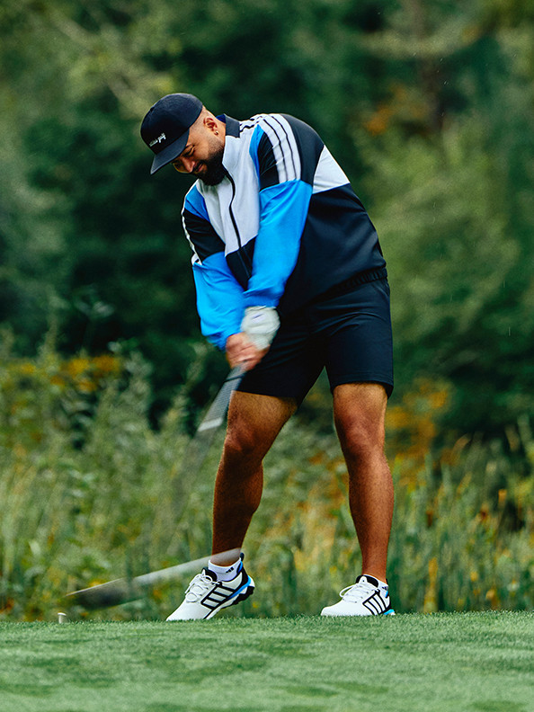 A person in athletic clothing is swinging a golf club on a grassy field surrounded by lush greenery.