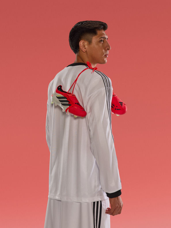 A person wearing a white sports jersey and red gloves stands against a bright red background.