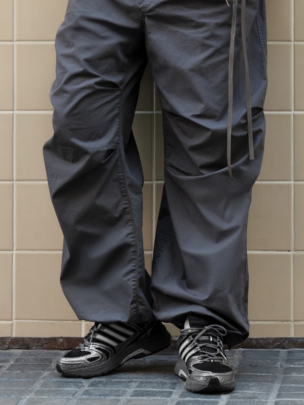The image shows a person's lower body wearing dark gray pants and black athletic shoes standing on a tiled floor.
