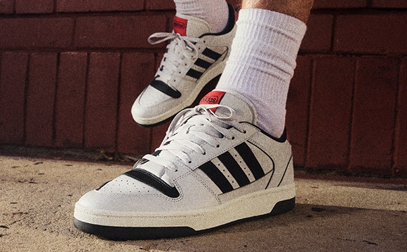 A pair of white and black sneakers with red accents stands in front of a brick wall.