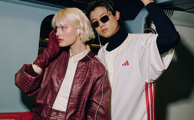 Two individuals, a woman with blonde hair and a man wearing sunglasses, are standing together in what appears to be a vehicle or transportation setting, with a dark background.