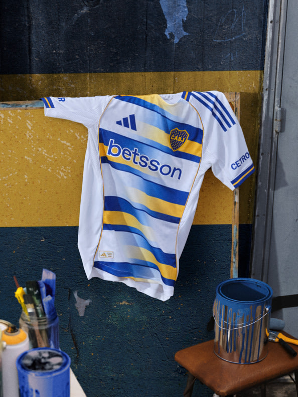 A white and blue sports jersey with the name "Betsson" prominently displayed hangs on a wall, surrounded by various objects in the background.