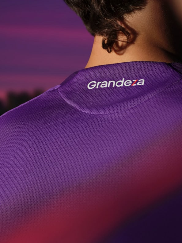 A person wearing a purple jersey with the "Grande-a" logo against a vibrant sunset sky.