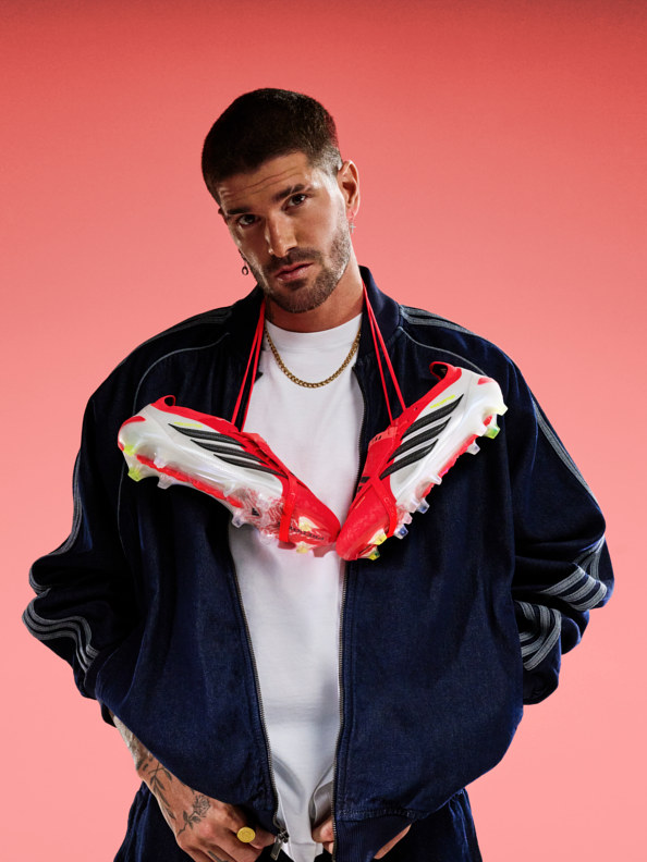 A young man wearing a navy blue jacket with red and white accents stands against a vibrant red background, his expression serious and focused.