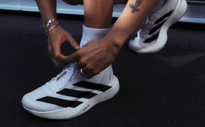 The image shows a person's lower body and feet, with the person wearing white and black athletic shoes and socks. The background appears to be a dark, shadowy environment.