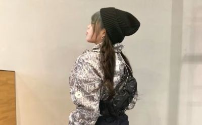 A person wearing a patterned jacket and a black beanie stands in a room with a wooden cabinet in the background.