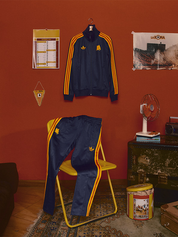 A navy blue tracksuit with orange stripes hangs on the wall, accompanied by a yellow chair and various other items in a cozy, vintage-inspired room setting.
