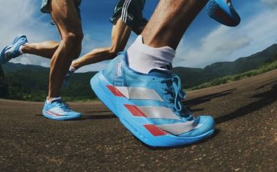 The image shows the lower body of a person running on a dirt road surrounded by mountains in the background.
