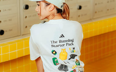 The image shows a person wearing a white t-shirt with the text "The Running Starter Pack" and various running-related icons printed on the back, standing in a hallway with yellow tiled walls.