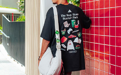 A person wearing a black t-shirt with a graphic design stands in front of a red tiled wall.