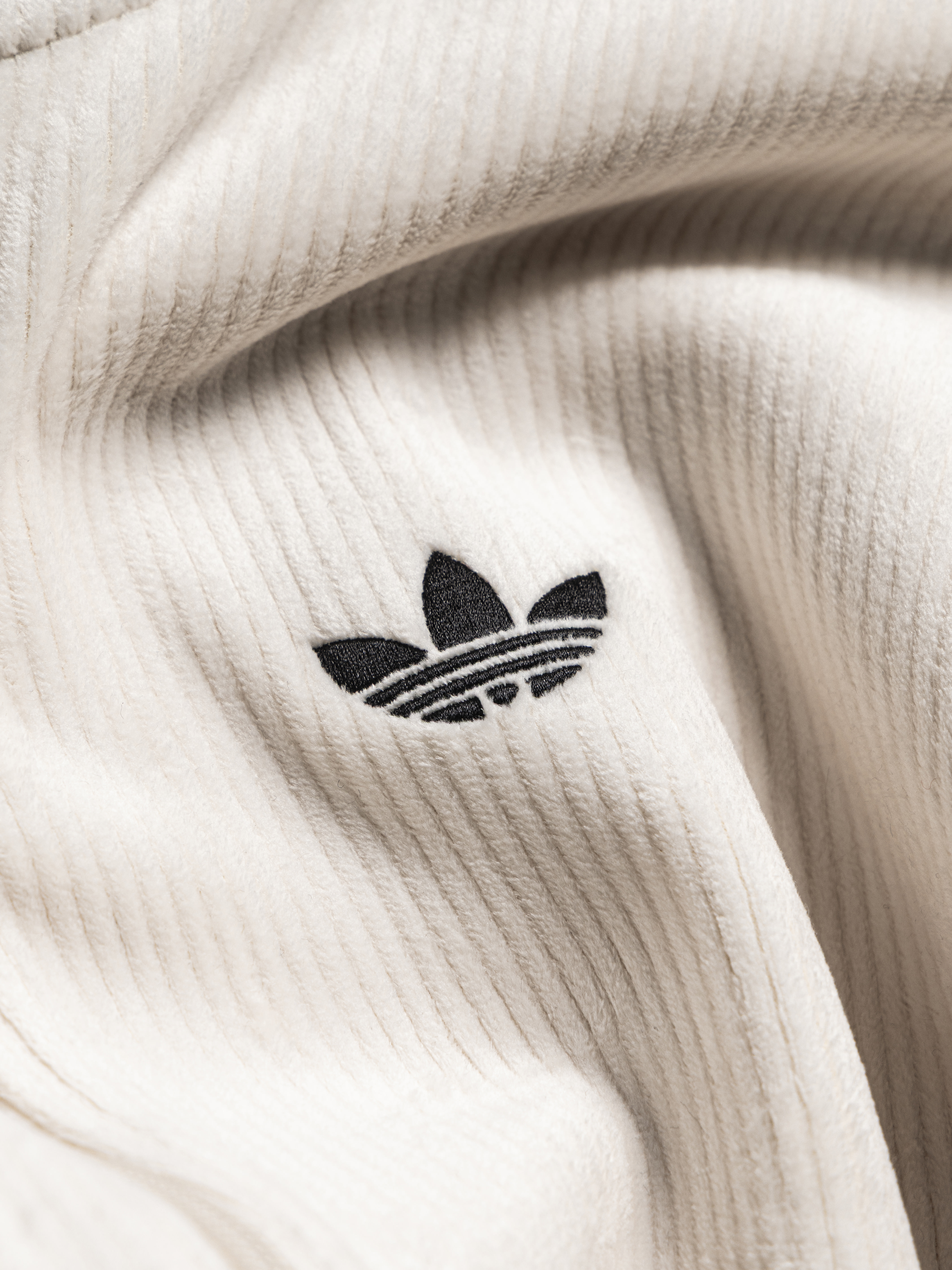 The image shows a close-up view of a white, ribbed fabric with the Adidas logo prominently displayed in the center.