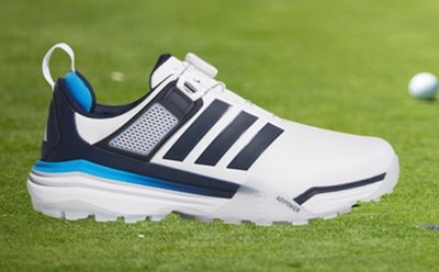 A white and blue athletic shoe with a thick sole sits on a lush green grass field, with a golf ball visible in the background.