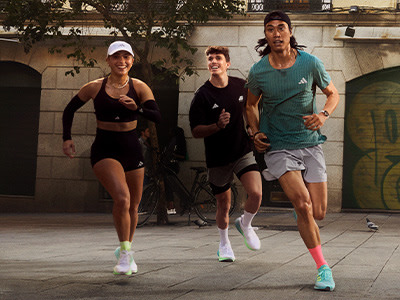 Three people, two women and one man, are jogging together on a city street at night, with buildings and trees visible in the background.