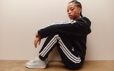 A young person wearing a black and white striped outfit is sitting on the floor against a plain beige wall.