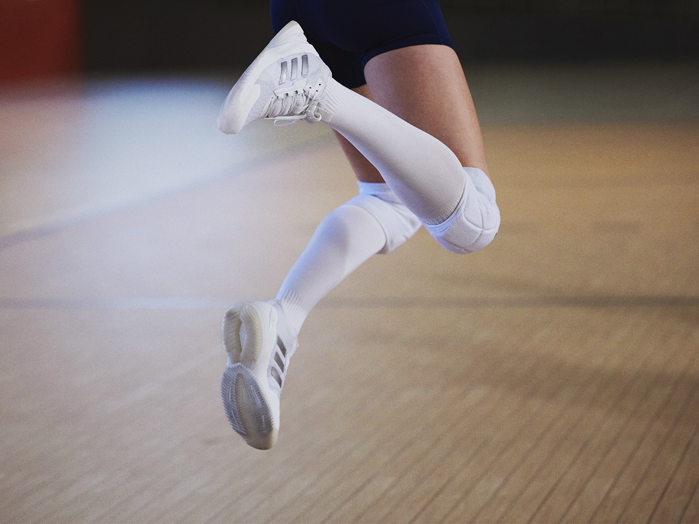 A person wearing white athletic shoes and socks is shown in mid-stride on a wooden floor.