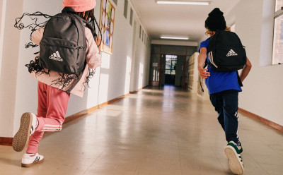 Dos personas con ropa deportiva de adidas están caminando por un pasillo, una persona en primer plano y la otra en el fondo.
