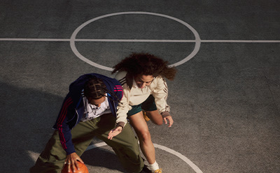 The image depicts two individuals, one with curly hair, engaged in a physical interaction within a circular structure on a dark background.