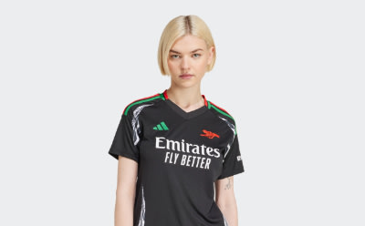 Une personne portant un maillot de football noir et vert se tient sur un fond blanc uni.