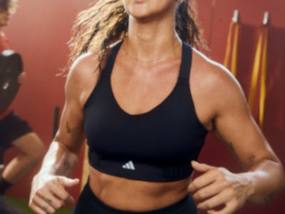 En kvinna som bär en svart sport-bh och shorts står i gymmet, med träningsutrustning synlig i bakgrunden.