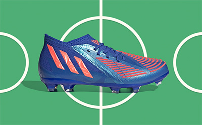 A blue and orange soccer cleat is displayed against a vibrant green background with white soccer field markings.