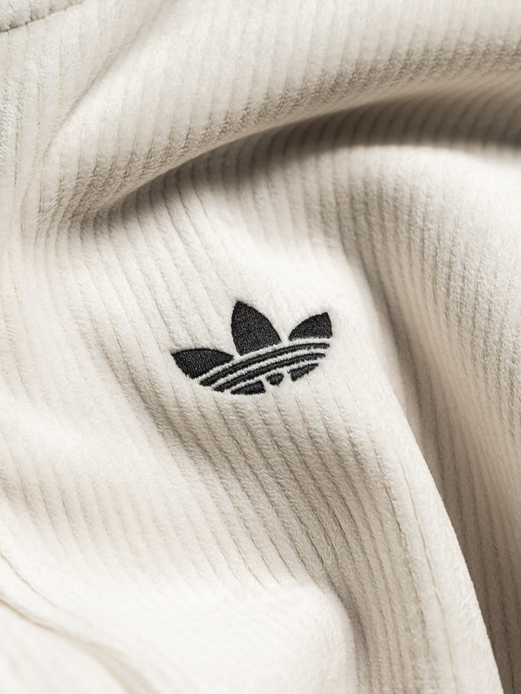 The image shows a close-up view of a white, ribbed fabric with the Adidas logo prominently displayed in the center.